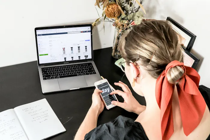 Woman who is looking at an ecommerce website Brisbane on a mobile device and has the website open also on a laptop. Photo from Unsplash.